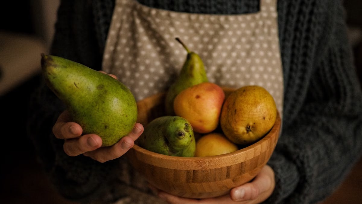Rustic image of hands holding a wooden bowl filled with pears, showcasing warmth and freshness.