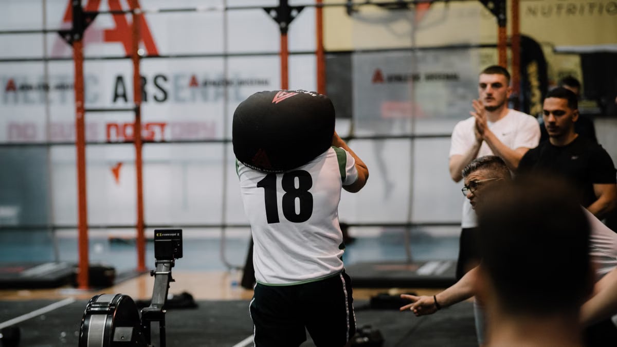 Athlete lifting a sandbag during a dynamic workout session in a gym, showcasing strength and focus.